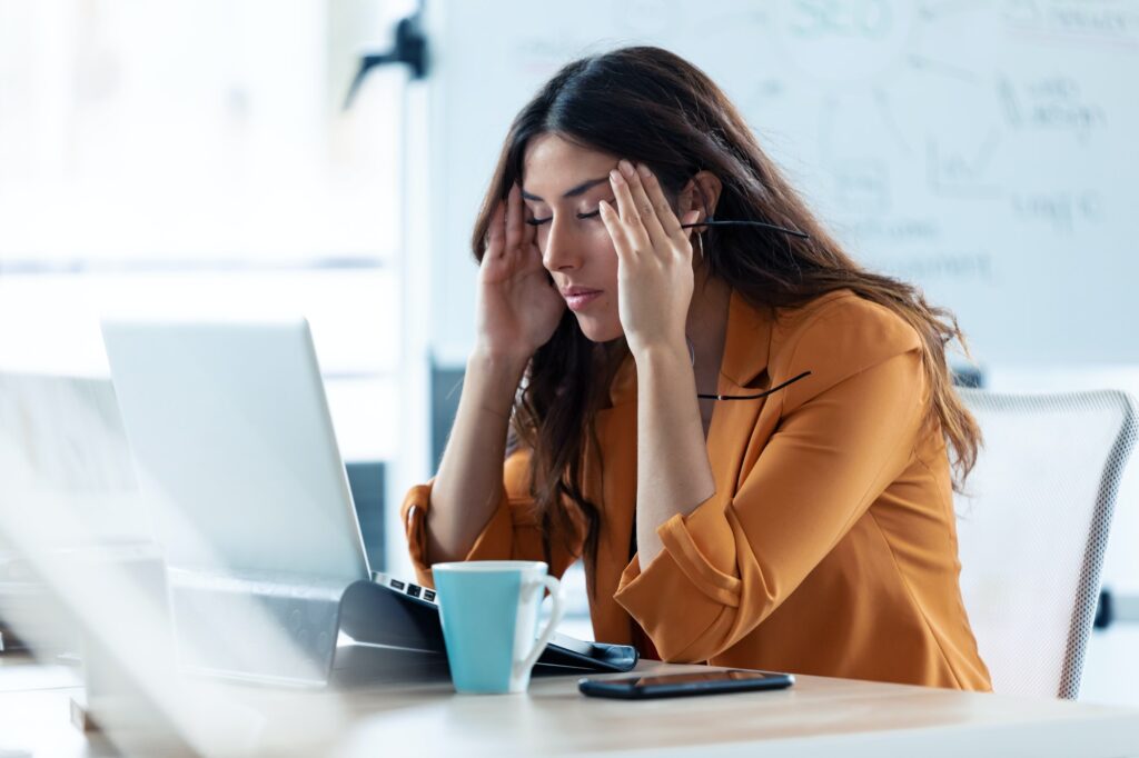 Jeune femme d'affaires avec un mal de tête travaillant avec un ordinateur portable dans un bureau.