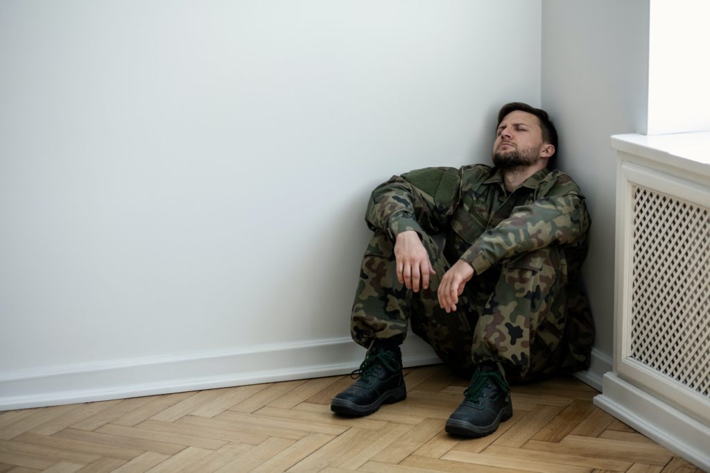Un militaire en uniforme, déprimé, assis dans le coin d'une salle vide.
