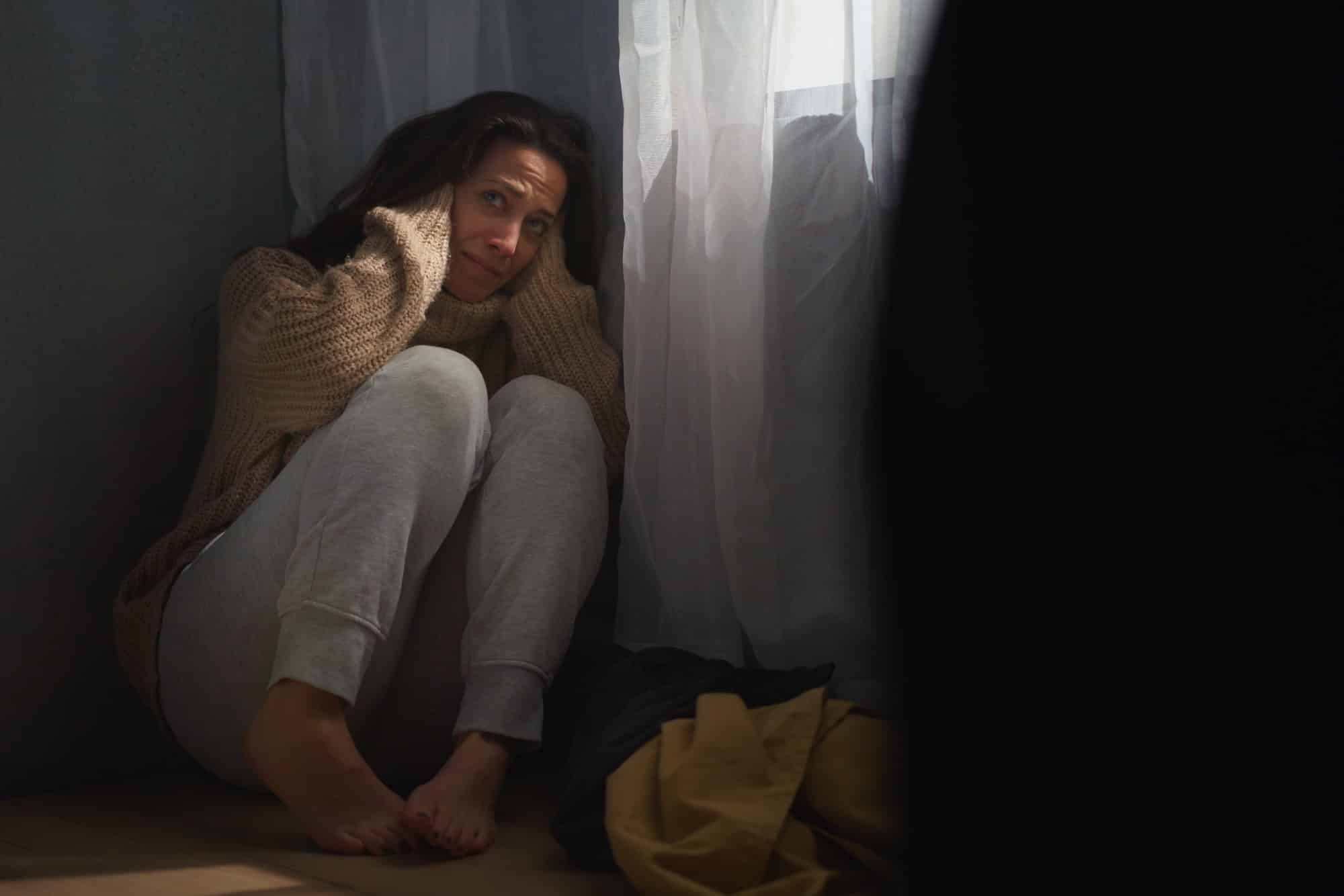 Une femme effrayée s'assoit sur le sol et se couvre la tête par crainte de violences domestiques